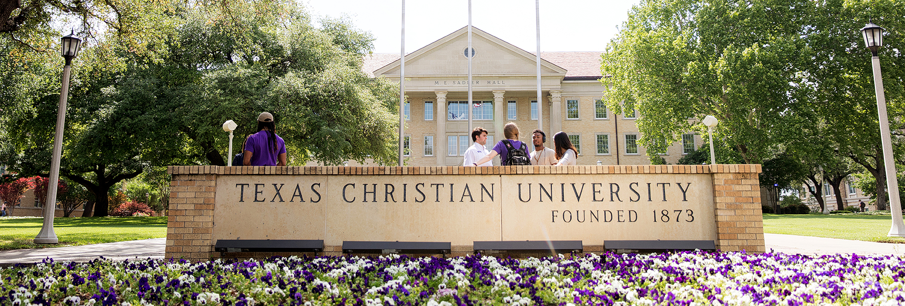 Section Image: Texas Christian University Sign in front of the building with flowers 